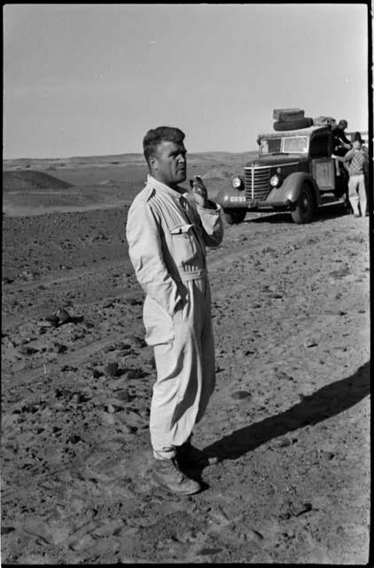 Expedition member standing, with others next to a truck in the background