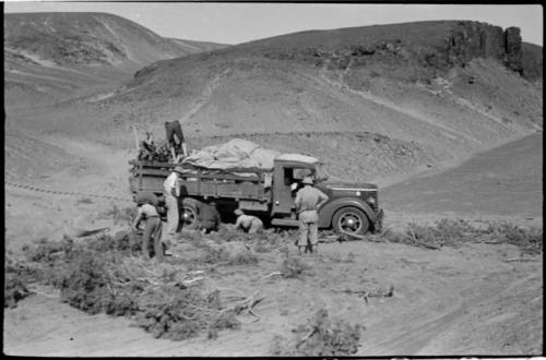 Expedition members putting brush under wheels of truck and retrieving something from the load