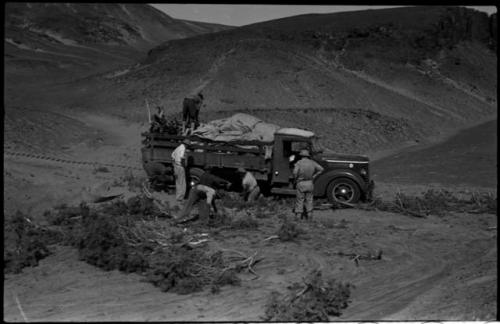 Expedition members putting brush under wheels of truck and retrieving something from the load