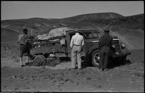 Expedition members standing and looking at the truck, with brush under the wheels, at the crest of a hill