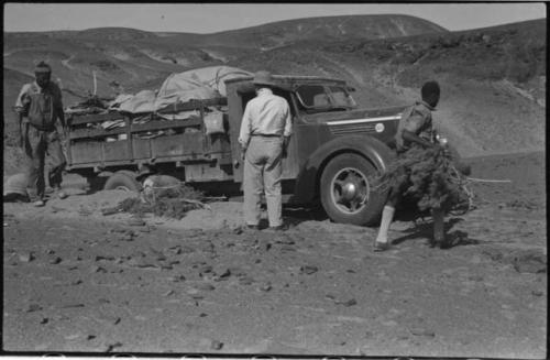 Expedition members standing and looking at the truck, with brush under the wheels, at the crest of a hill