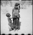 Woman carrying a child on her back, and another child standing next to her