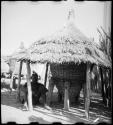 Person sitting next to a storage basket covered with a thatched roof