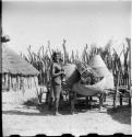 Woman standing in her kraal next to storage baskets