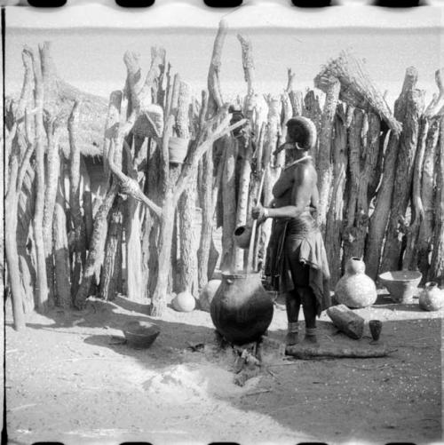 Woman stirring something in a large pottery cooking pot on the fire