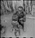 Man sitting, holding cigarettes and showing his filed teeth, and a child standing in front of him