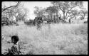 Ju/'hoansi walking with trucks in the background