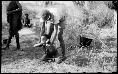 /Gishay ("Old Gau's" son) holding Little ≠Gao who is crouched on the ground, struggling