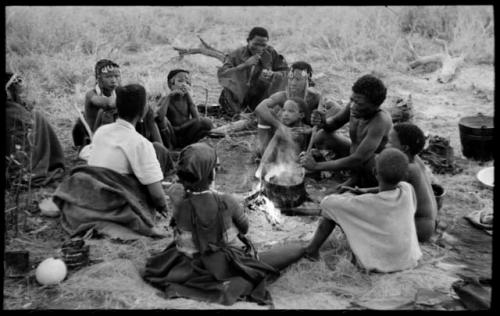 //Kushay, "Little ≠Gao", !Ungka, and other unidentified people seated around a pot on a fire while "Old Gau" stirs the pot