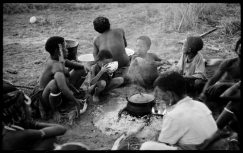 //Kushay, "Old Gau," !Ungka, and other unidentified people seated around a pot on a fire and "Little ≠Gao" drinking from a bowl