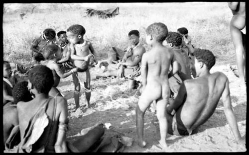 Debe, !Ungka Norna and Bau with a rope, Elizabeth Marshall Thomas taking notes, and other unidentified people; part of Elizabeth Marshall Thomas's child study