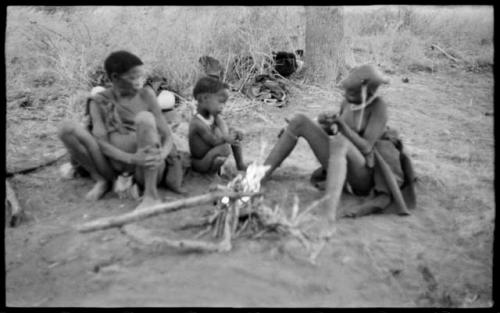 /Naoka (!U's mother), !Ungka Norna, and an unidentified, visiting girl beside a fire