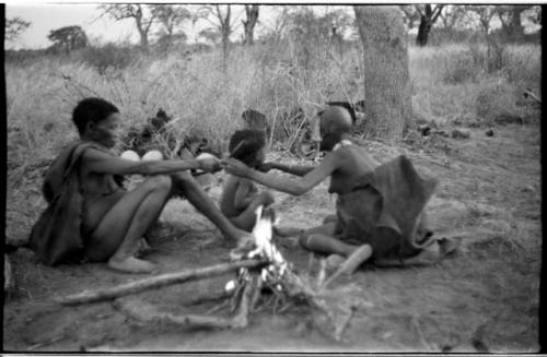 /Naoka (!U's mother), !Ungka Norna, and an unidentified, visiting girl beside a fire