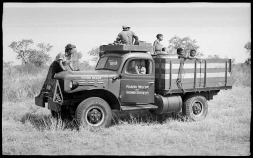 Power wagon with Elizabeth Marshall Thomas on the fender, Kernel Ledimo on top, John Marshall driving, and unidentified Ju/'hoansi on the back