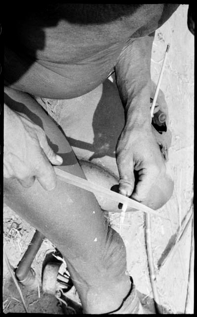 Person's hands scraping arrow shaft with a knife