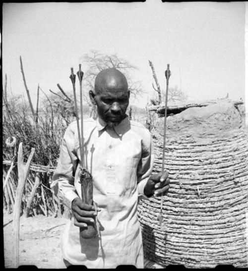 Man holding arrows with metal points and feathered ends, two of them in a quiver