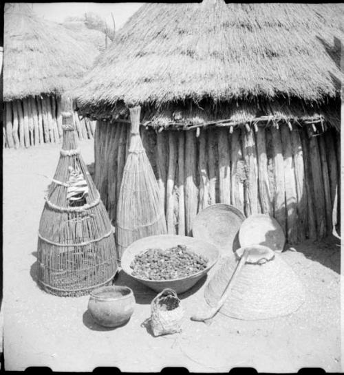 Fish traps, baskets and food in front of a hut