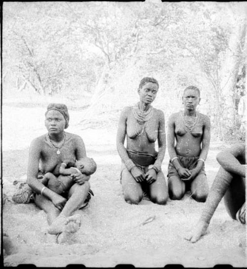 Woman sitting and nursing a baby, and two women kneeling