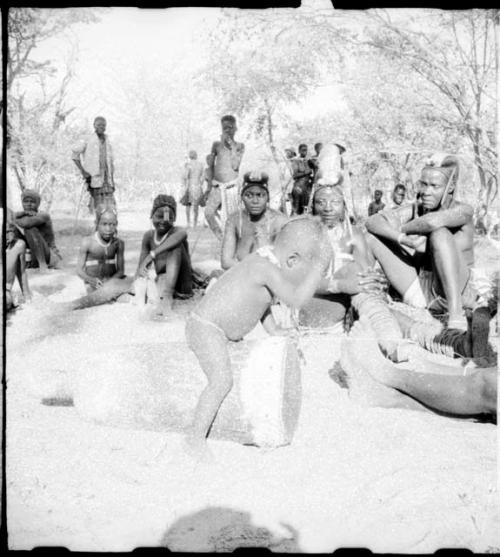 Child playing a drum, and people sitting and watching