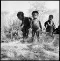 Two children standing, with women sitting in background