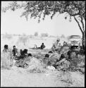 People sitting and reclining near Nicholas England at recording equipment and Chevrolet, long shot