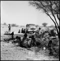 People sitting and reclining near Nicholas England at recording equipment and Chevrolet, long shot