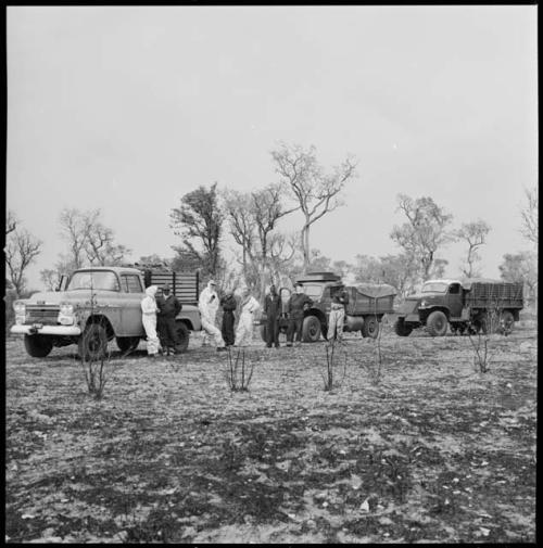 Expedition members standing near line of trucks and wearing clothing and head coverings to protect against tsetse flies