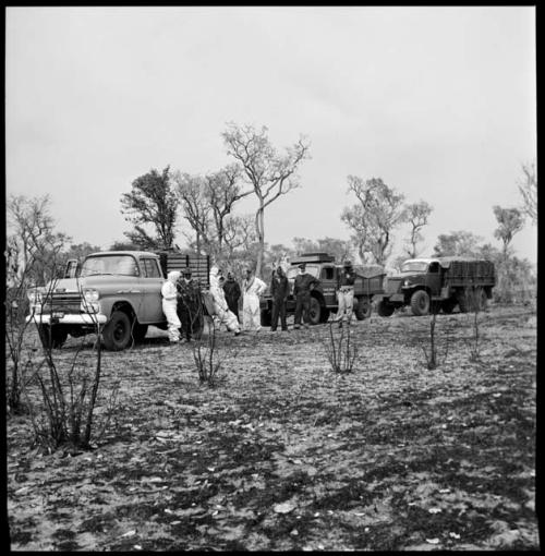 Expedition members standing near line of trucks and wearing clothing and head coverings to protect against tsetse flies