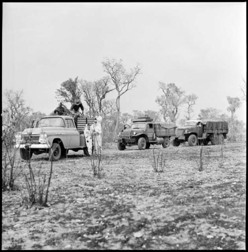 Expedition members wearing clothing and head coverings to protect against tsetse flies, and standing near line of trucks