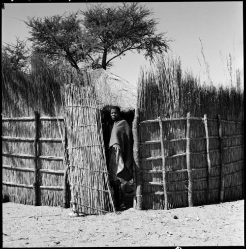 Woman standing at the partially opened gate of a hut compound