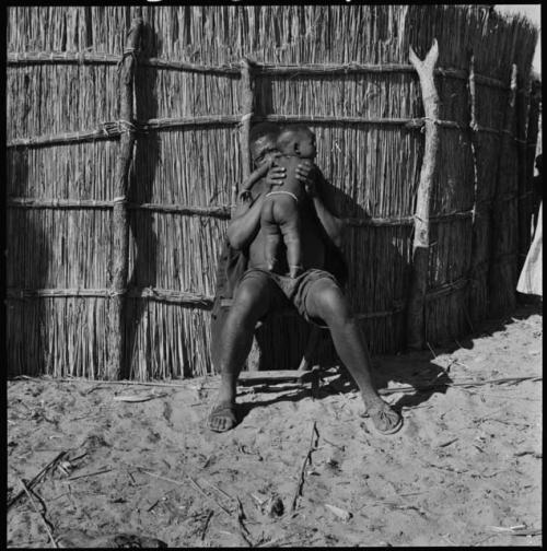 Man sitting next to a fence and holding a baby