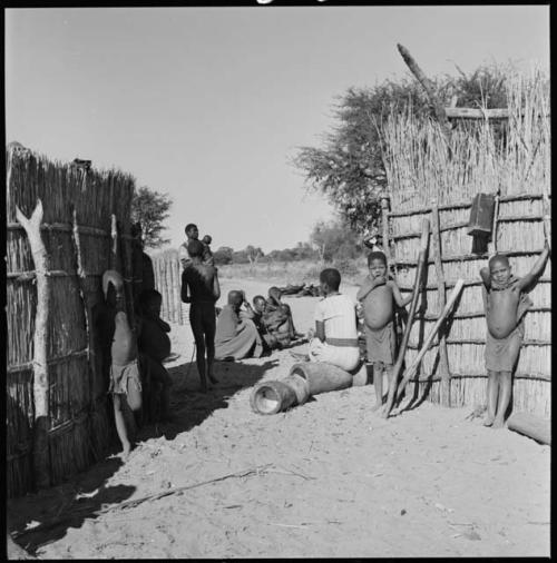 Group of children standing between two fences, with Rose sitting on a pestle that is lying on the ground