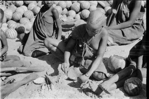 Girl pounding tsama melon seeds in a piece of gourd used as a receptacle