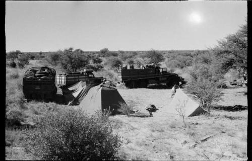 Expedition members setting up tents, expedition trucks in background