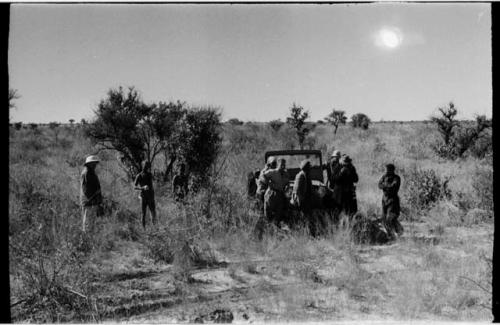 Oukwane, !Gai, and expedition members standing around expedition Jeep