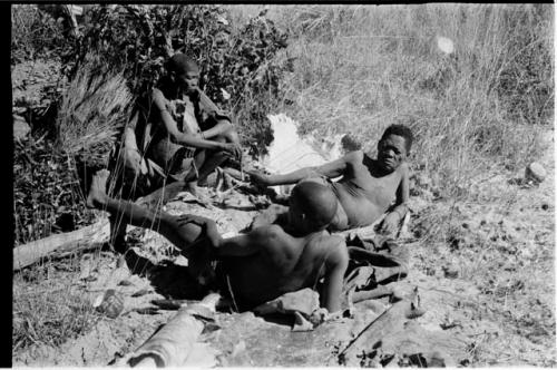 Oukwane and !Gai reclining; /Twikwe passing a pipe to Oukwane