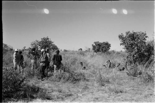 Group of people standing with expedition members, watching gemsbok butchering, distant view