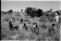 Group of people sitting with expedition members in the grass, John Marshall filming in the background