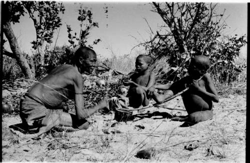 /Twikwe, /Gaiamakwe, and !Ou/ke sitting playing musical bow