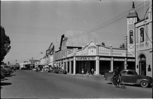 Man riding a bicycle down the street, and people standing in front of a store