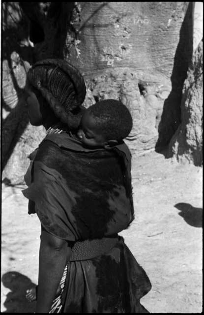 Woman carrying a baby on her back, with baobab tree in background