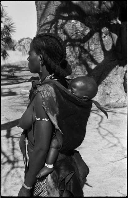 Woman carrying a baby on her back, with baobab tree in background