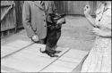 Woman and man standing next to a dog doing a trick, the woman is holding a treat for the dog