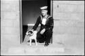 Man in a sailor uniform kneeling next to a dog, in a doorway