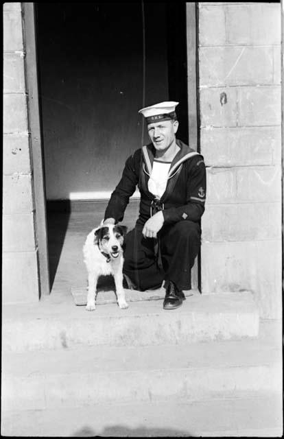 Man in a sailor uniform kneeling next to a dog, in a doorway