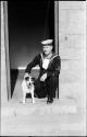 Man in a sailor uniform kneeling next to a dog, in a doorway