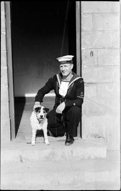 Man in a sailor uniform kneeling next to a dog, in a doorway