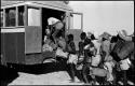 Large group of people standing in line next to trucks