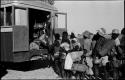 Large group of people standing in line next to trucks