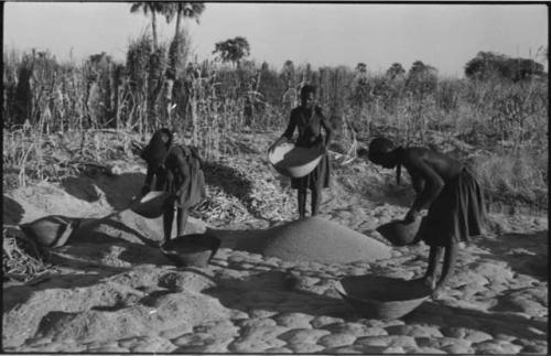 Three women standing and holding baskets of grain